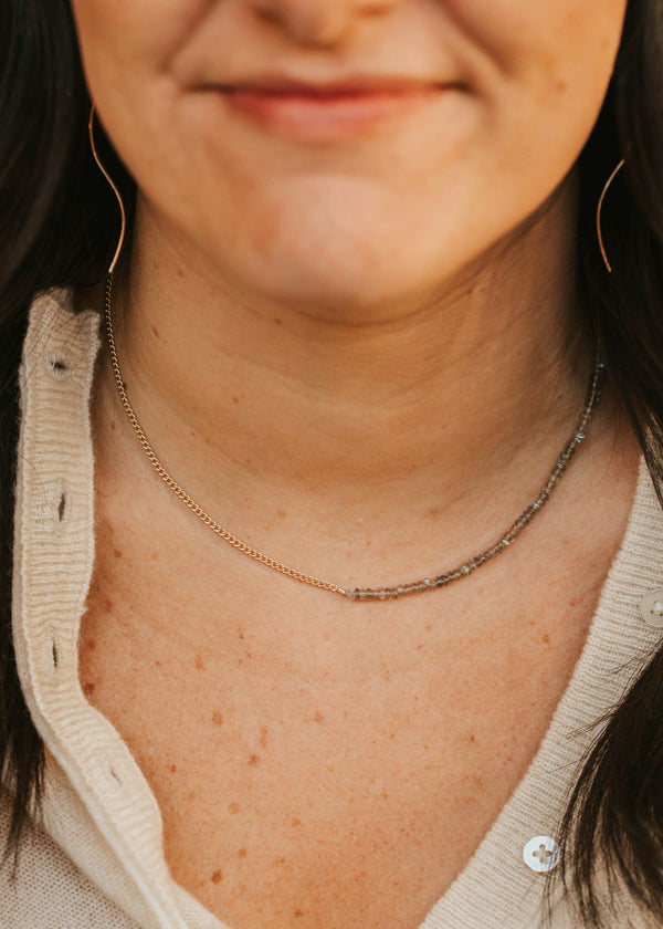 Close-up of a person wearing a gold necklace with a neutral background