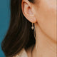Close-up of a person wearing gold earrings against a blue background
