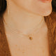Woman wearing a gold necklace with a small pendant, smiling.