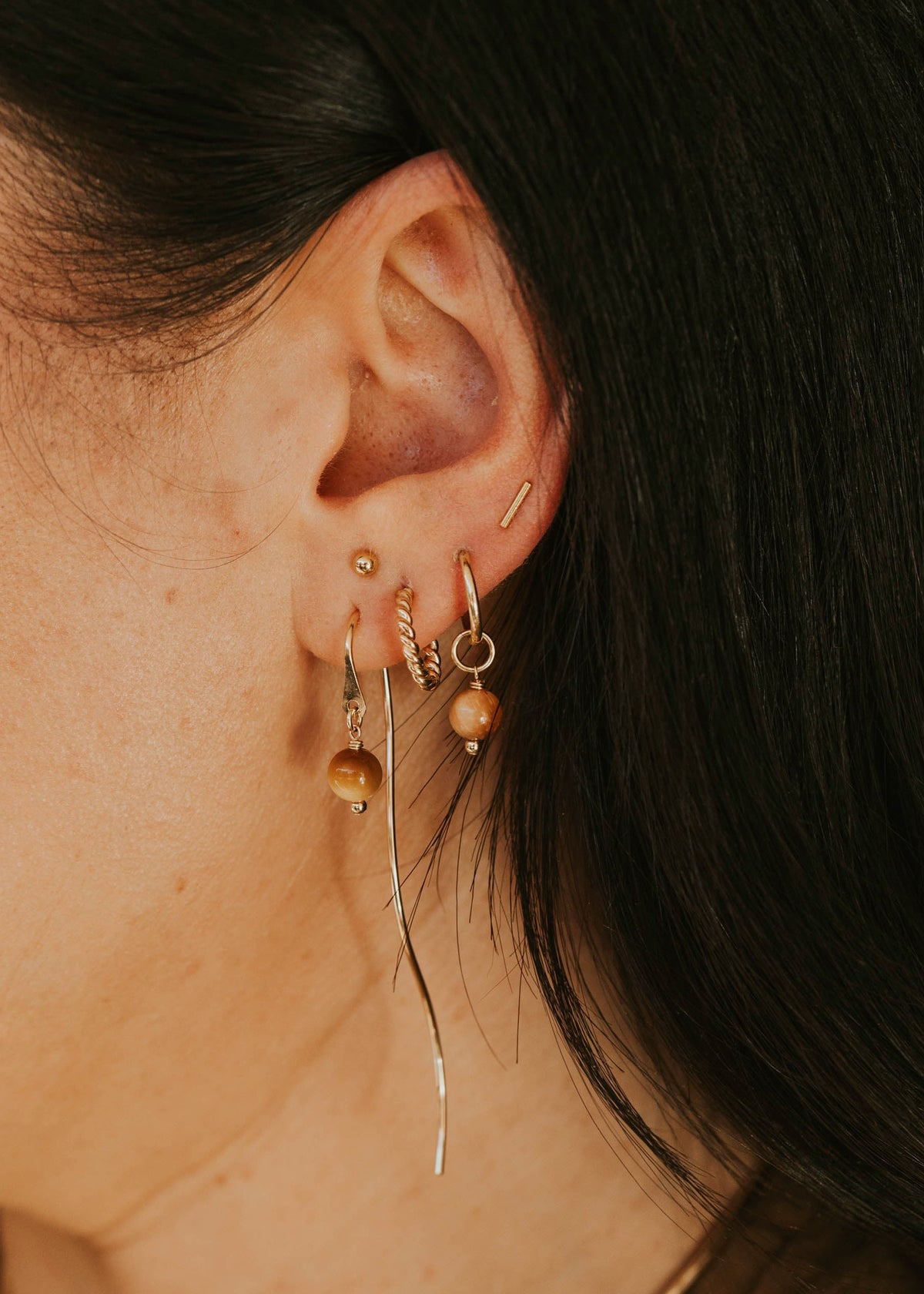 Close-up of an ear with gold earrings against a dark background