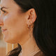 Woman wearing gold earrings and a necklace with a blurred background
