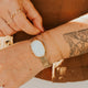 Close-up of a person's wrist with gold bracelet and rings, wearing a brown jacket.