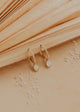 Gold hoop earrings with opal stones on a textured beige surface