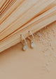 Silver earrings with gemstones on a textured beige surface