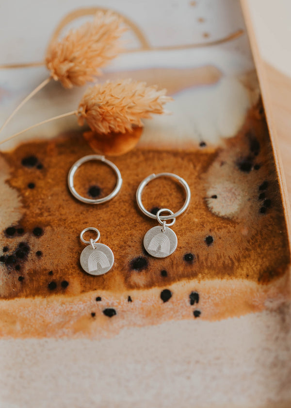 sterling silver rainbow hoop charm earrings on a dish