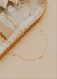Gold necklace on a textured beige surface with a dish in the background