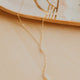 Gold necklace on a beige surface with a decorative dish in the background