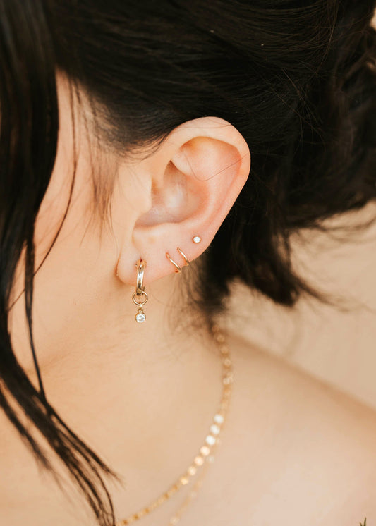 Close-up of an ear with gold hoop earrings and a necklace, with blurred background