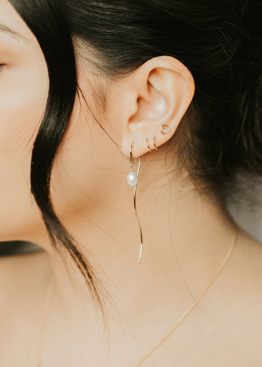 Close-up of a person wearing a delicate earring with a pearl drop.