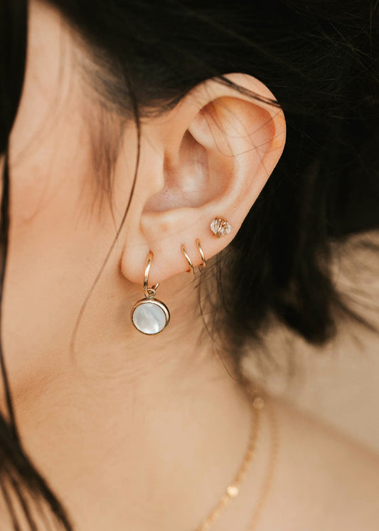 Close-up of an ear with gold earrings and a necklace against a neutral background