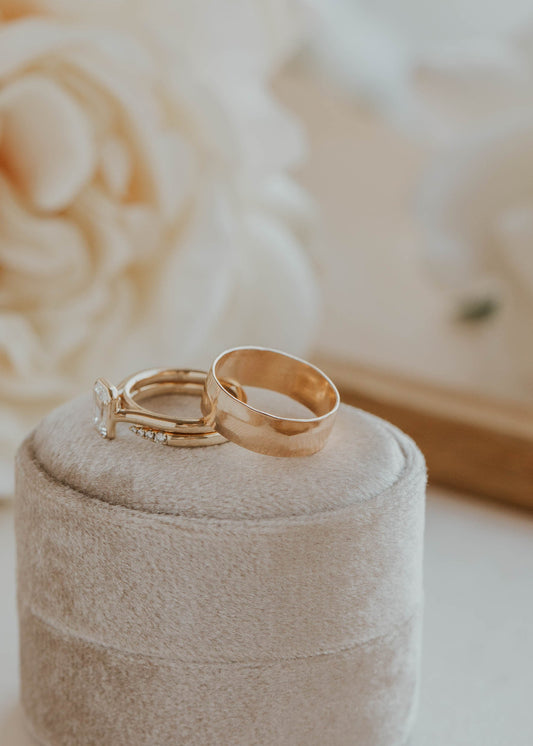 Two gold rings on a beige jewelry box with a blurred floral background
