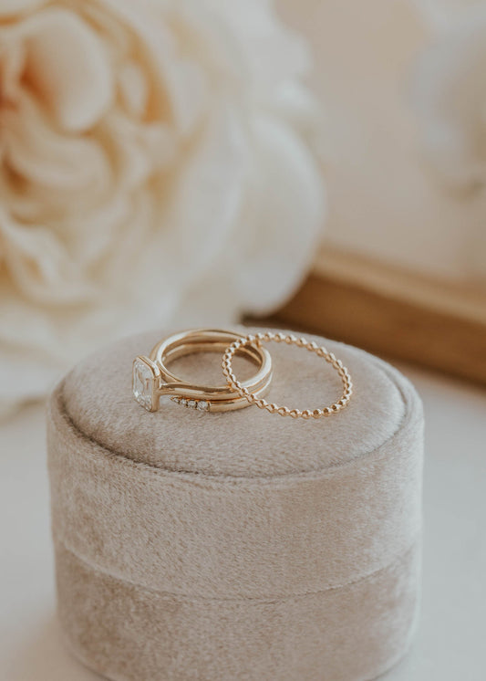 Two gold rings on a beige jewelry box with a blurred floral background