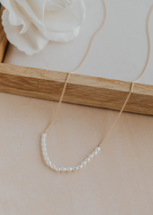 Pearl necklace on a beige surface with a white flower in the background