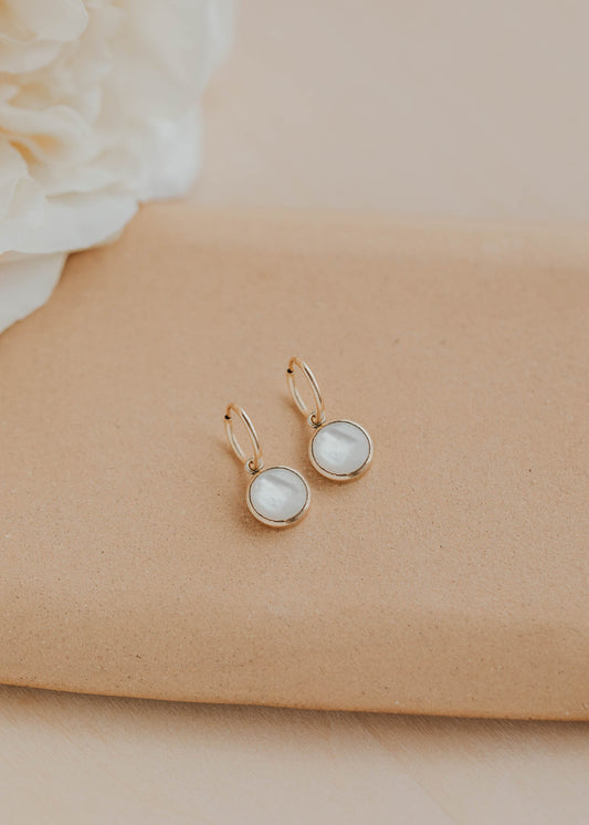 Pair of earrings with round gemstones on a beige surface with a white flower in the background