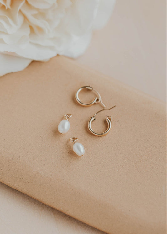 Gold hoop and pearl earrings on a beige surface with a white flower.
