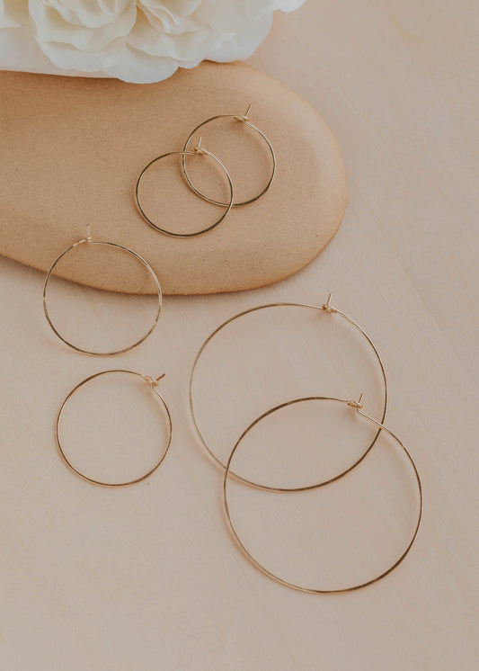 Gold hoop earrings on a beige surface with a white flower in the background