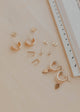 Collection of gold earrings on a beige surface with a ruler for scale.