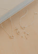 Silver jewelry set including necklaces and earrings on a beige surface.