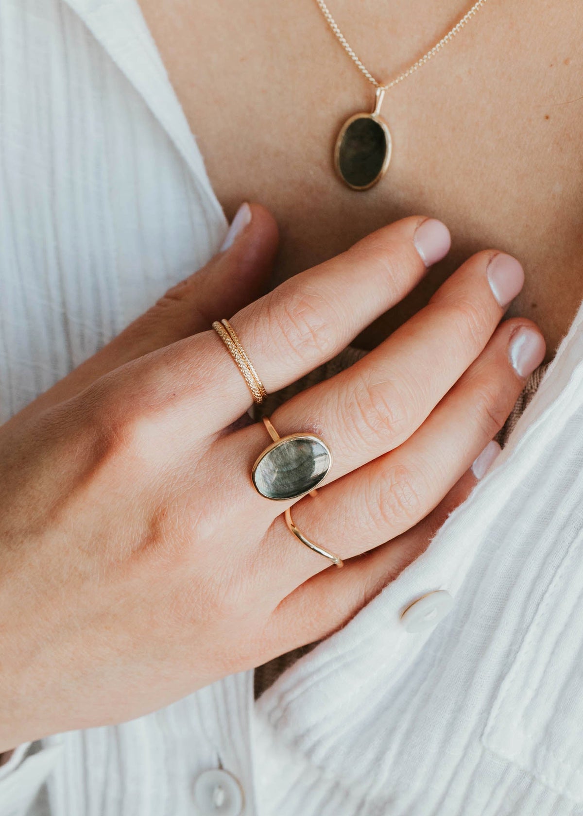 Close-up of a person wearing gold necklaces and rings with green stones.