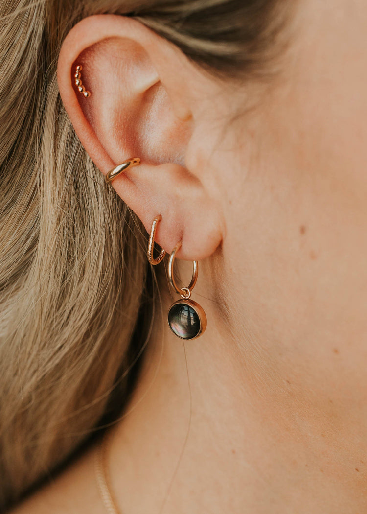 Close-up of an ear wearing gold hoop earrings with a black gemstone.