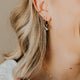 Close-up of a person wearing earrings and a necklace with a neutral background