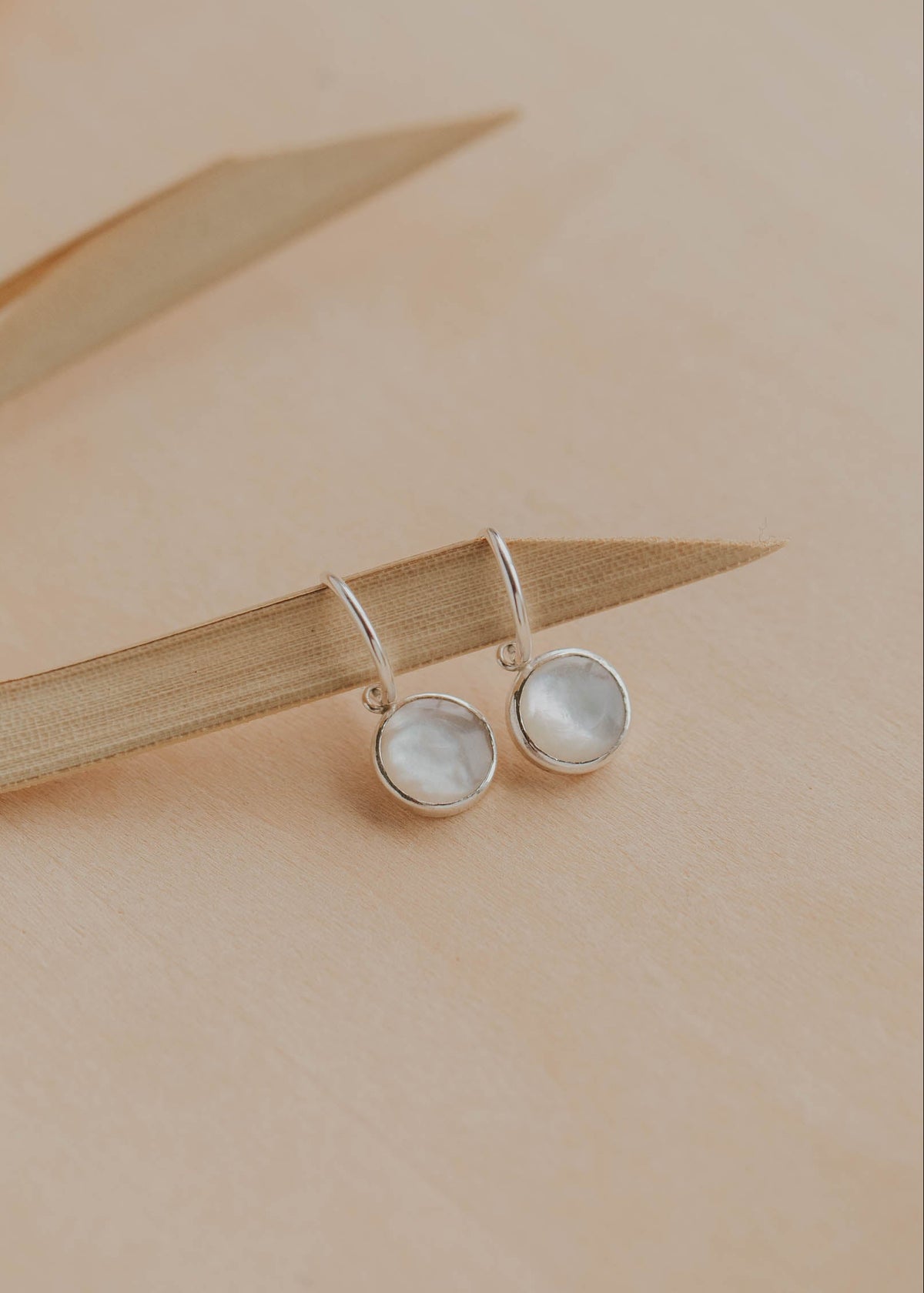 Pair of silver earrings with round gemstones on a beige background