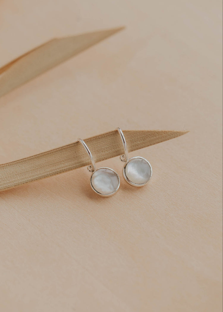 Pair of silver earrings with round gemstones on a beige background