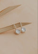 Pair of silver earrings with round gemstones on a beige background