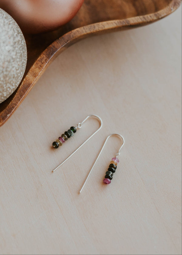 Pair of beaded earrings on a neutral surface with decorative ornaments in the background.
