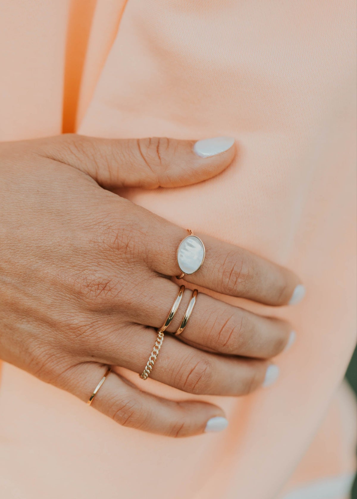 Hand wearing multiple rings on a soft peach background
