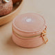 Pink jewelry box with gold zipper on a beige surface with decorative spheres in the background