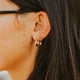 Close-up of an ear wearing gold hoop earrings with dark hair.