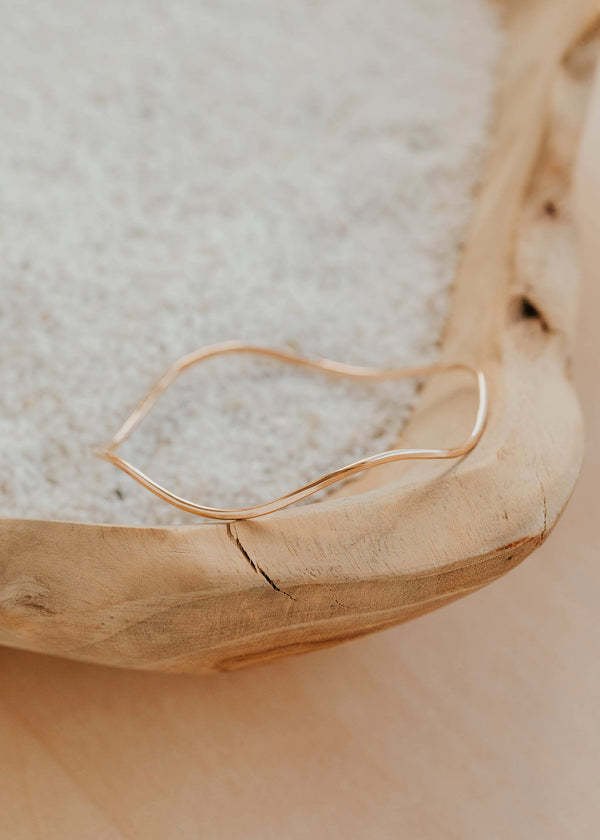Gold bangle bracelet on a textured surface with a wooden bowl