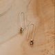 Pair of U-shaped threader earrings on a sandy surface