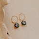 Gold hoop earrings with black stones on a beige surface