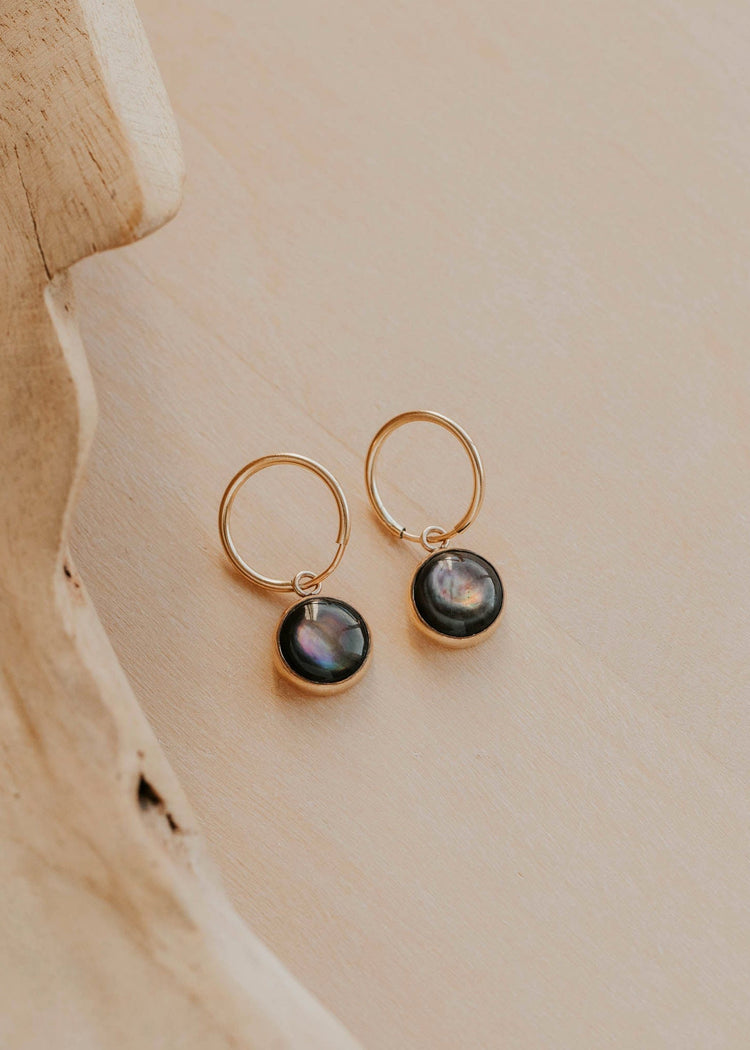 Gold hoop earrings with black stones on a beige surface
