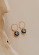 Gold hoop earrings with black stones on a beige surface