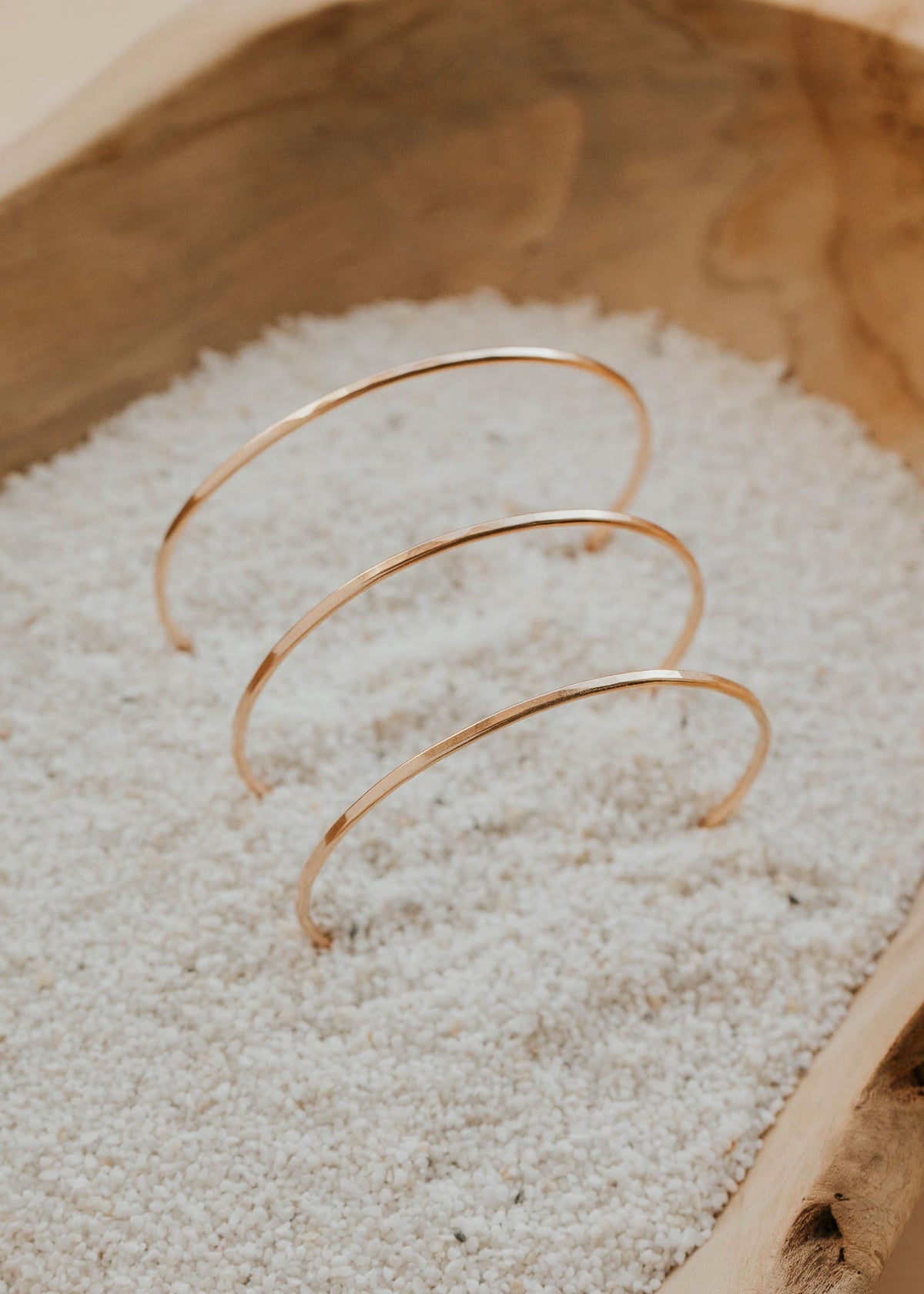 Gold bracelet on a bed of sand inside a wooden bowl