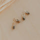 Three small decorative charms on a beige surface with a leafy branch in the background.