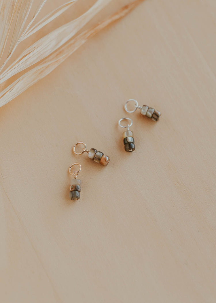 Three small decorative charms on a beige surface with a leafy branch in the background.