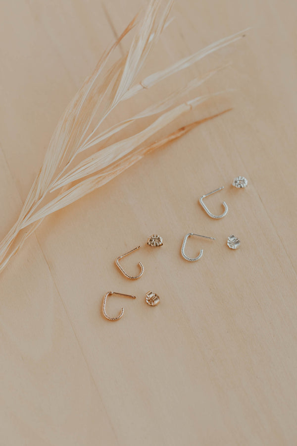 Gold and silver earrings on a beige surface with dried grass