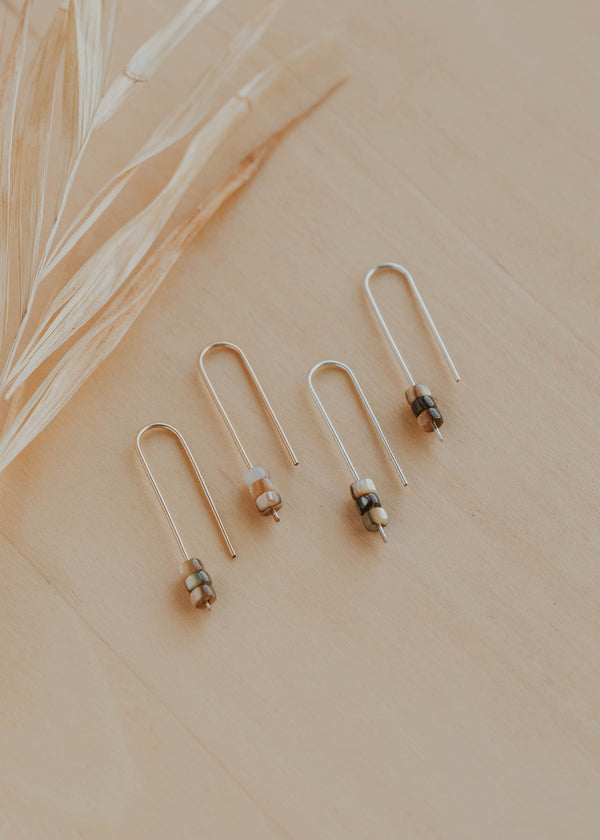 Pair of gold earrings with small beads on a beige surface with dried grass.