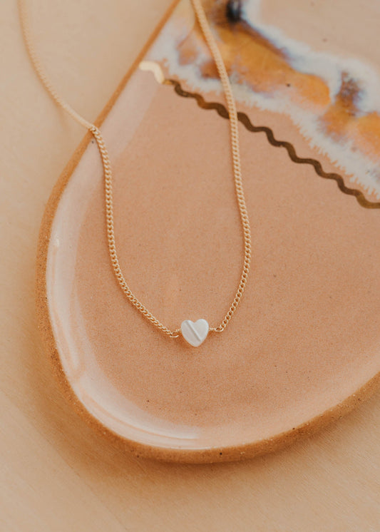 Gold necklace with a heart pendant on a ceramic plate