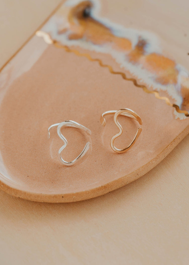Gold and silver heart-shaped rings on a beige ceramic dish with a marble pattern.