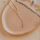 Gold necklace with a small diamond pendant on a beige plate
