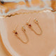 Gold earrings with red gemstones on a beige surface