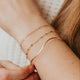Close-up of a person's wrist with gold bracelets and rings on a neutral background