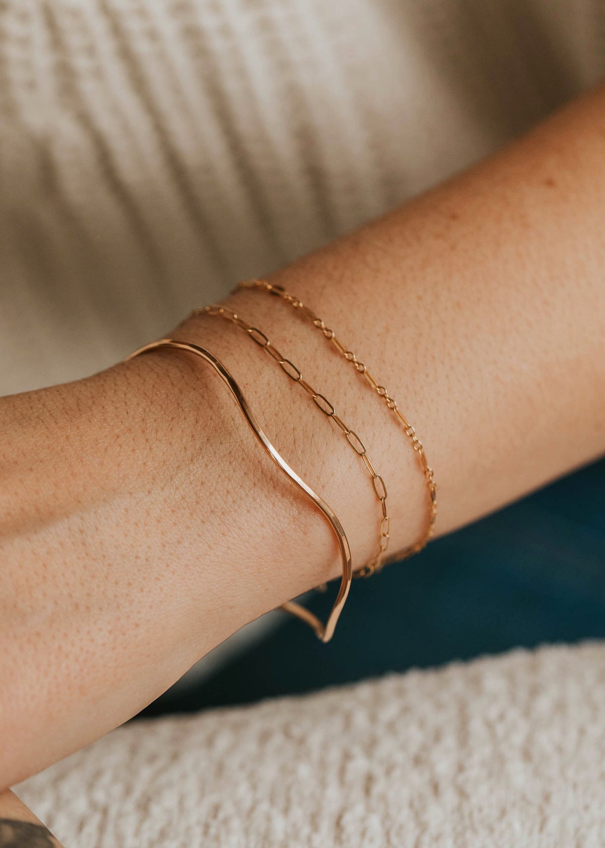 Close-up of a person's wrist wearing gold bracelets on a neutral background