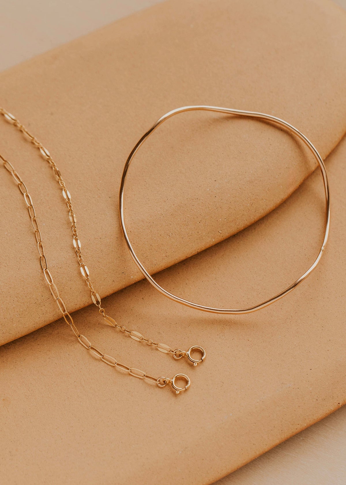 Gold bracelet and chain on a beige surface