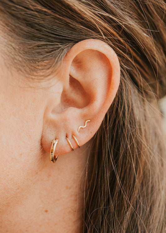 Close-up of an ear wearing gold hoop earrings with a blurred background